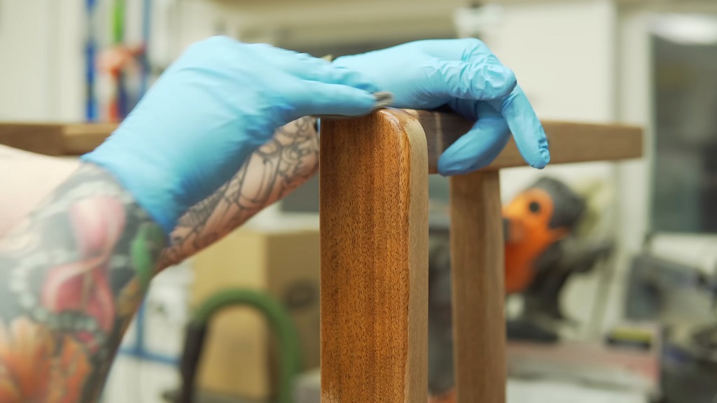 Čovek sunđerom nanosi vosak za negu drveta na nogu od stolice