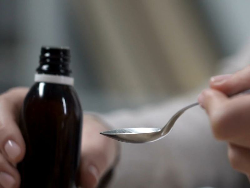 osoba drži sirup za iskašljavanje i kašičicu u rukama