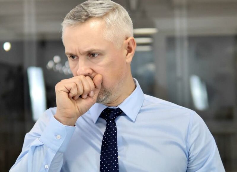 prikaz muškarca u košulji sa kravatom koji kašlje i drži ruku na ustima