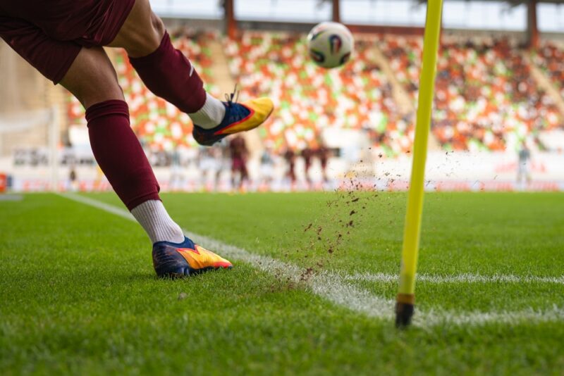 Fudbaler izvodi korner udarac dok lopta leti sa ivice terena pored zastavice